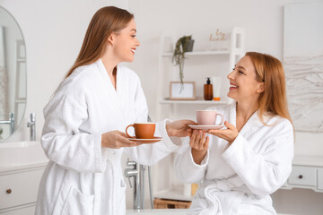 Young woman with her mother drinking coffee after shower in bathroom - Powered by Adobe