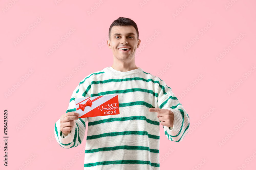 Poster Young man pointing at gift voucher on pink background