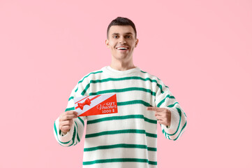 Young man pointing at gift voucher on pink background