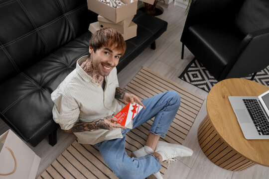 Young tattooed man with gift voucher sitting at home