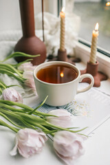 Cup of tea, bouquet of pink tulips and candles, spring aesthetics