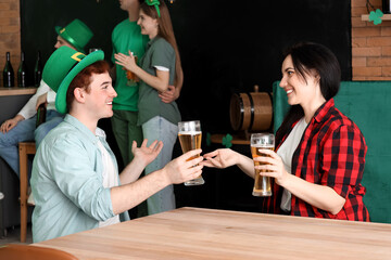 Young couple with beer celebrating St. Patrick's Day at table in pub