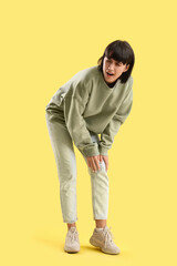 Naklejka premium Young woman suffering from knee pain on yellow background