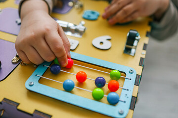 Busy Board. A child plays with pleasure with a toy model at home, which is intended for the development of fine motor skills