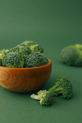 Broccoli in a wooden bowl on a green background