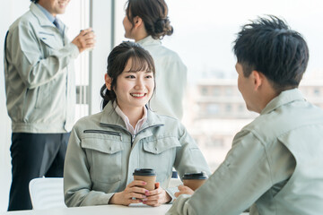 オフィスの休憩所でコーヒーを飲む作業着姿の女性と男性
