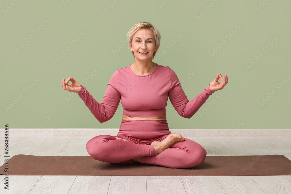 Sticker Portrait of meditating mature woman sitting on floor against green wall