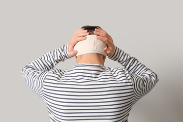 Young man with brain concussion and bandaged head on light background, back view