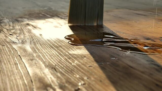 Oil and varnish for wood. brush spreads oil on a wooden surface.Treating wood with oil or varnish.Brush on the surface of a wooden table in the sun.Protecting the wooden surface from damage. 