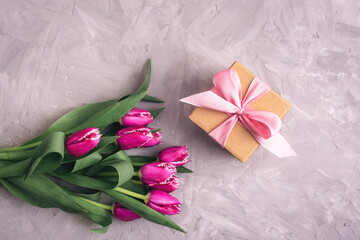 Pink tulips and gift in a box on gray textured table. Spring festive background, top view, flat lay