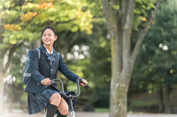 公園の中を自転車通学する制服姿の中学生・高校生の女の子
