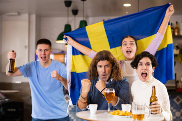 Group of happy friends, sports supporters cheering for favorite team with flag of Sweden while...