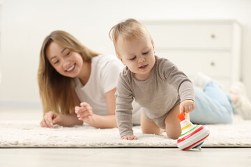Children toys. Happy mother and her little son playing with spinning top on rug at home, selective...