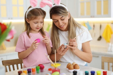 Obraz na płótnie Canvas Easter celebration. Mother with her cute daughter painting eggs at white marble table in kitchen