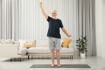 Senior man doing exercise with fitness elastic band on mat at home