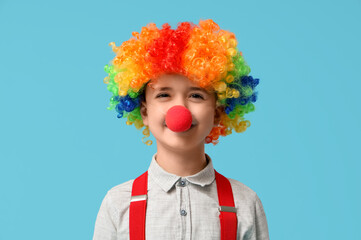 Funny little boy in clown wig and nose on blue background. April Fools Day celebration