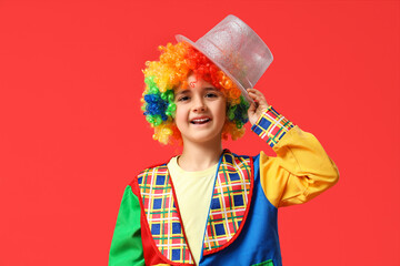 Funny little boy in clown costume with hat on red background. April Fools Day celebration