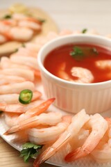 Tasty boiled shrimps with cocktail sauce, chili and parsley on light wooden table, closeup