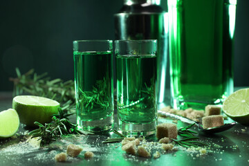 Absinthe in shot glasses, spoon, brown sugar, lime and rosemary on gray table, closeup. Alcoholic...