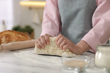 Obraz na płótnie Canvas Making bread. Woman kneading dough at white table in kitchen, closeup