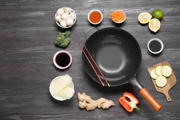 Fotobehang Empty iron wok and chopsticks surrounded by ingredients on dark grey wooden table, flat lay. Space for text © New Africa