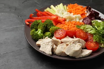 Fotobehang Balanced diet and healthy foods. Plate with different delicious products on black table, closeup © New Africa