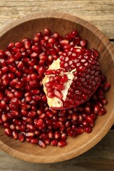 Ripe juicy pomegranate grains in bowl on wooden table, top view