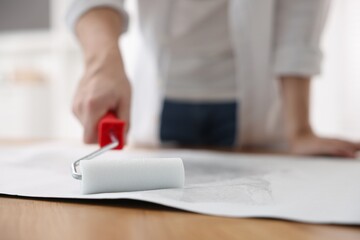 Man applying glue onto wallpaper sheet at table indoors, closeup