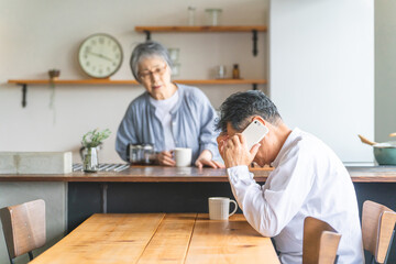 家でスマホで電話しながら困る高齢者男性(謝る・ショック・詐欺・悩む)
