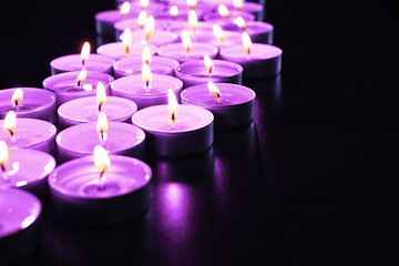Beautiful burning violet candles on black background. Funeral attributes