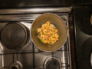 Round bottom frying pan with stir fry of shrimp on gas burner of stove with warm white overhead lighting