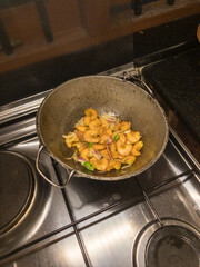 Round bottom frying pan with stir fry of shrimp on gas burner of stove with warm white overhead lighting