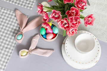 Easter eggs with tulips and dinnerware on dining table, top view