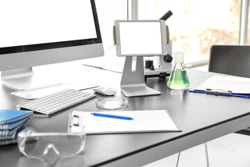 Blank tablet computer with chemistry flask on table in laboratory, closeup