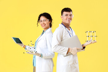 Young chemists with molecular models and tablet computer on yellow background