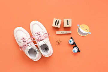 Shoes with tied together laces, fake spiders and calendar on orange background. April Fools Day...