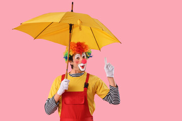 Portrait of clown with umbrella pointing up on pink background. April Fool's day celebration