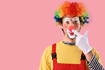 Portrait of clown touching his red nose on pink background. April Fool's day celebration