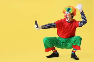Portrait of funny clown taking selfie on yellow background. April Fool's day celebration
