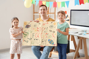 Father holding April Fools Day poster with his children at home
