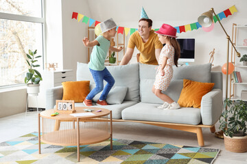 Father and his children with party hats having fun at home. April Fool's Day celebration