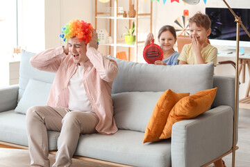 Little children surprising their father with whoopee cushion at home. April Fool's Day prank