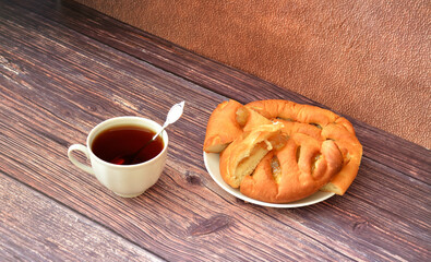 A cup of hot tea with a spoon and a plate with slices of fresh apple pie on a wooden table.