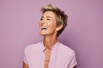Portrait of a happy young woman laughing against a purple background.