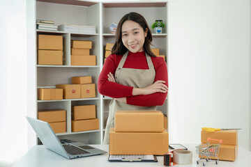 of freelance Asian woman wearing apron using laptop and boxes to receive and review online orders to prepare packs to sell to customers, SME small business entrepreneur, online SME business concept