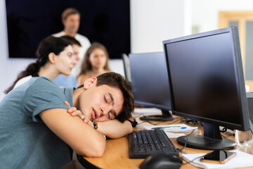 Exhausted young employee engaged in software development at IT startup in coworking space sleeping...