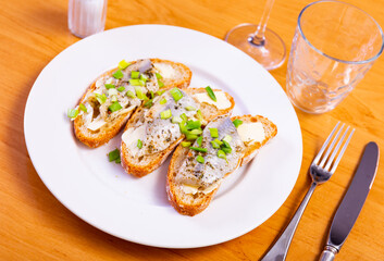 On top of greased bread is slices of lightly salted herring. Sandwiches with butter and fish, decorated with ring of green onion