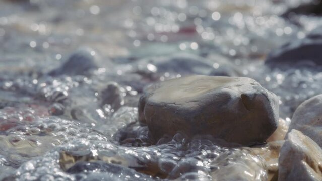River water splashes over rocks on the shore. Slow motion, close up.
