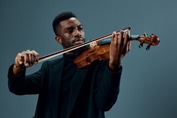 Soulful African American musician in black suit playing violin on gray background in elegant...