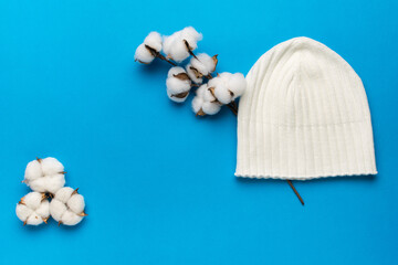 Fototapeta na wymiar A cotton twig and a white knitted hat on a blue background.